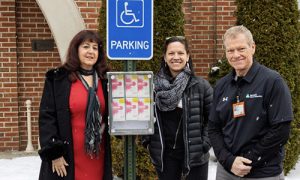 Three people standing in snow next to handicap parking sign.