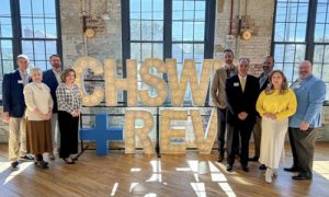 Group of people standing next to large lit sign in modern venue with large windows.
